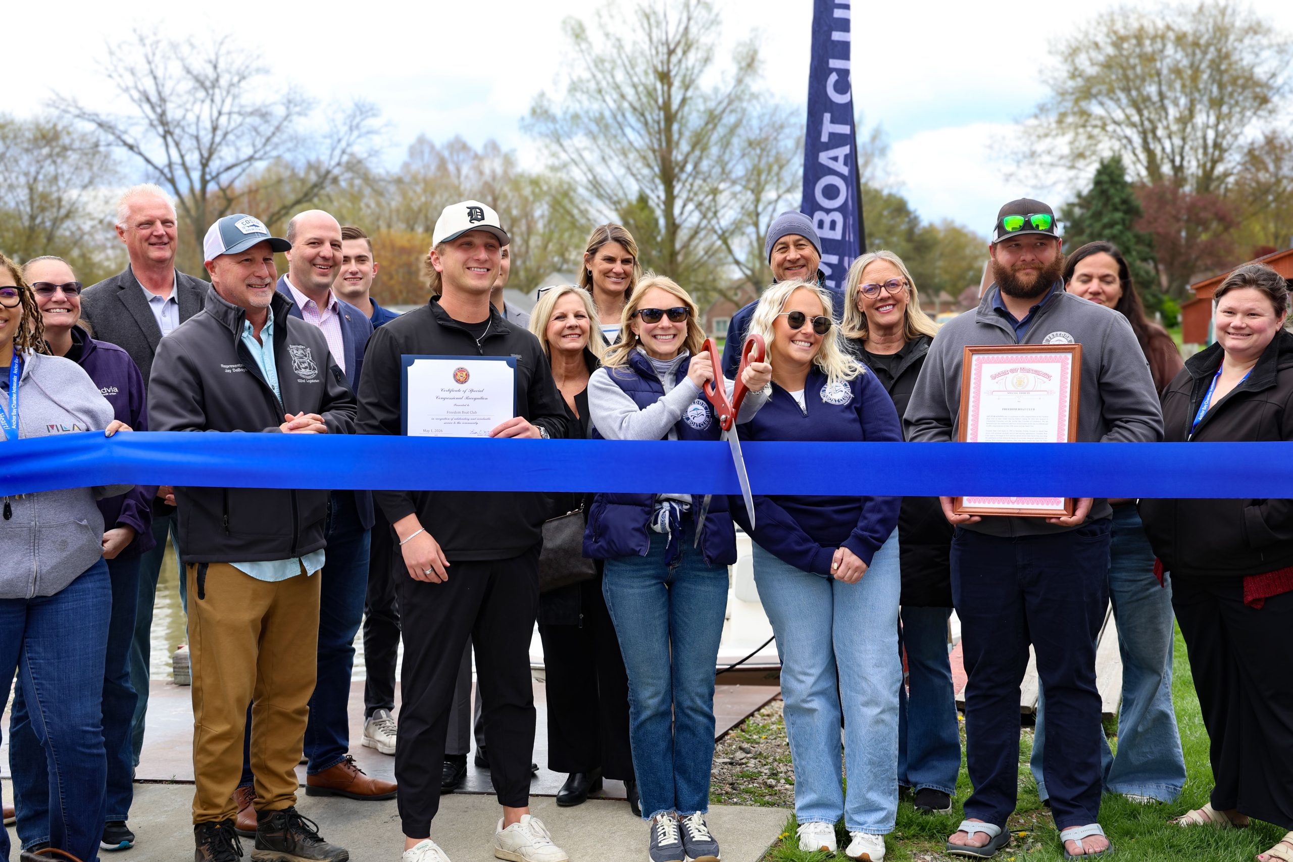A group of people at a ribbon cutting ceremony holding a legislative tribute. Sen Hertel is in the photo welcoming the Freedom Boat Club to Chesterfield Township