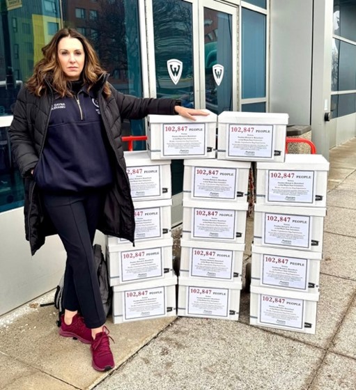 Sen Polehanki standing next to stacked boxes filled with petitions to Wayne State University 