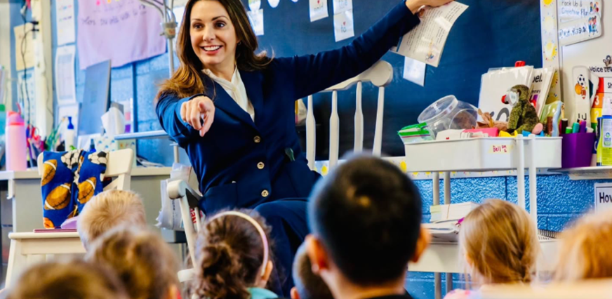 Sen Polehanki pointing at a board and a group of children in a classroom