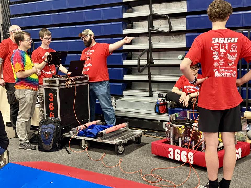 A group of highschool students driving a robot at a robotics competition