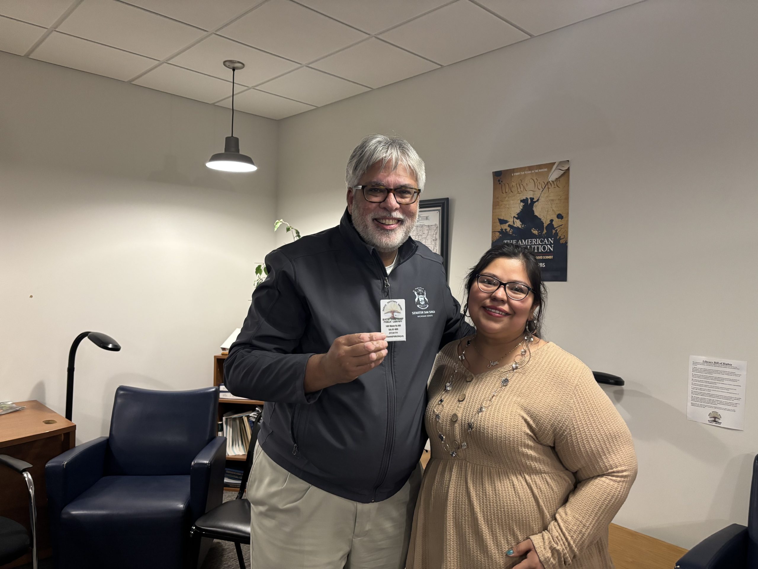 Senator Singh standing with a constituent while. holding up his library card
