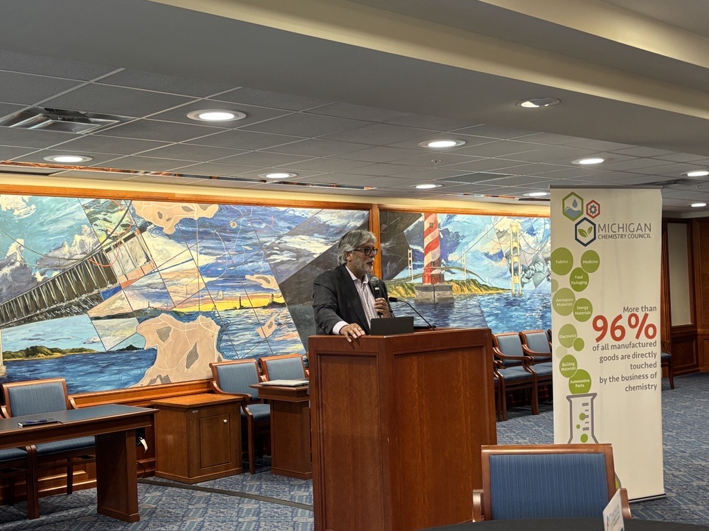 Sen. Singh speaking at a podium with members of the Michigan Chemistry Council
